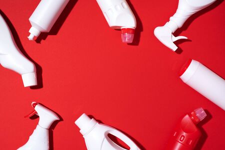 Composition with plastic bottles of cleaning products over red background. Top view. Flat lay. Copy...