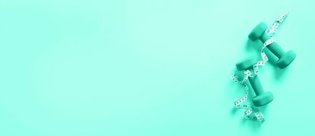 Fitness, sport concept with dumbbells and measuring tape over mint color background. Trendy green...