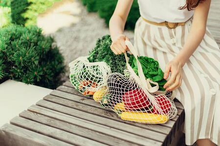 Girl holding mesh shopping bag and cotton shopper with vegetables without plastic bags, wooden background. Zero waste, plastic free concept. Sustainable lifestyle. Bannerの写真素材