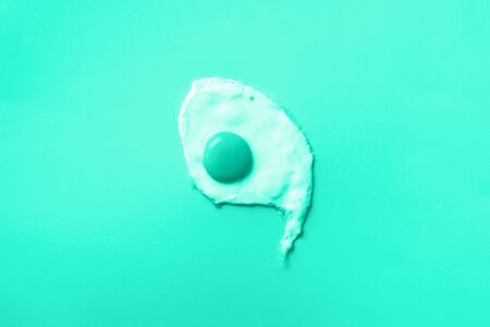One fried egg on mint color background. Trendy green and turquoise color. Creative food concept in minimal style. Top view.の写真素材