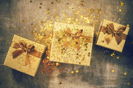 Christmas gift box with golden stars and sparkles on grey bacground. Gift box tied with golden...