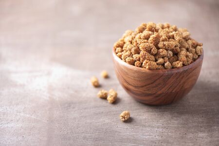White dried mulberry in wooden bowl on wood textured background. Copy space. Superfood, vegan, vegetarian food concept. Macro of mulberry berries, selective focus. Healthy snack.の写真素材