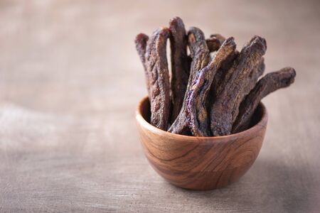 Sun dried bananas in wooden bowl on wood textured background. Copy space. Superfood, vegan, vegetarian food concept. Macro of bananas texture, selective focus. Healthy snack.の写真素材
