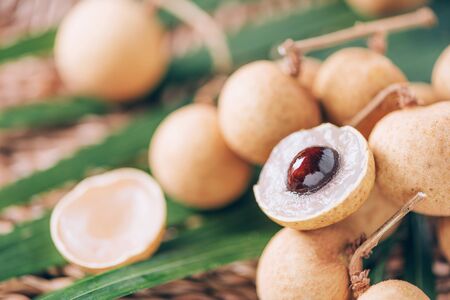 Longan fruits over palm leaves on rattan background. Copy space. Dimocarpus longan. Bunch of exotic longans. Tropical food conceptの写真素材