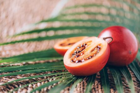 Tamarillo fruit or terong belanda with palm leaves on rattan background. Copy space. Tropical travel, exotic fruit. Vegan and vegetarian conceptの写真素材