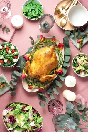 Festive family dinner table. Serving plates, bowls with salads and vegetables dishes, snack, whole roasted chicken, eucalyptus flowers on pink shabby background. Valentine day, Women's Day, mother's day, wedding brunch, festive family lunch and dinner concept.の写真素材