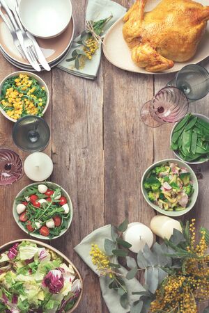 Festive family dinner table. Serving plates, bowls with salads and vegetables dishes, snack, whole roasted chicken, eucalyptus, mimosa flowers on wooden background. Valentine day, Women's Day, mother's day, wedding brunch, festive family lunch and dinner conceptの写真素材