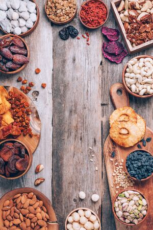 Mix of dried fruits and nuts -brazil nuts, cashew, pecan, almonds, macadamia, pine nuts, hazelnuts, pineapple, raisins, dates, dried apricots, goji, papaya, figs, mulberry on wooden background.Top view. Superfood, vegan, vegetarian concept.の写真素材