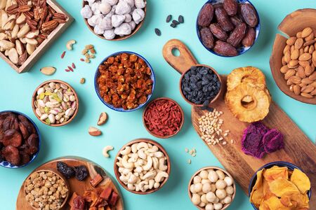 Assortment of nuts and dried fruits - brazil nuts, cashew, pecan, almonds, macadamia, pine nuts, hazelnuts, pineapple, raisins, dates, dried apricots, goji, papaya, figs, mulberry on blue background. Top view. Superfood, vegan, vegetarian concept.の写真素材