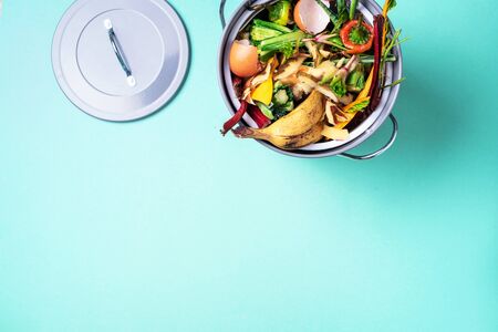 Recycle kitchen waste. Sustainable and zero waste living. Vegetable waste in recycling compost pot. top view. Copy space. Peeled vegetables on chopping board, white compost bin on blue backgroundの写真素材