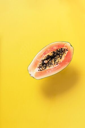 Halved papaya on yellow background. Top view. Copy space. Summer time. Tropical travel, exotic fruit. Vegan and vegetarian concept.の写真素材