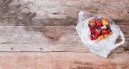 Moldy and wrinkled rotten peppers in plastic bag on wooden background. Concept of unhealthy,...