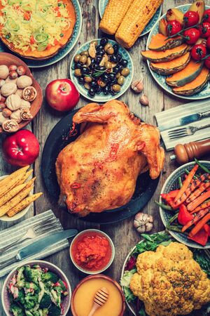 Thanksgiving dinner cooking preparation. Traditional dishes: chicken, pumpkin, corn, vegetables salads over wooden background. Top view, copy space. Autumn harvest, organic vegetables. Family dinner.の写真素材