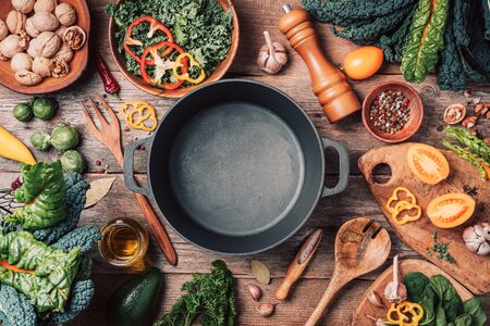 Various organic vegetables ingredients and empty iron cooking pot, wooden bowls, spoons on wooden background. Top view, copy space. Organic vegetables ingredients for vegan cooking. Clean eating food, zero waste concept.の写真素材
