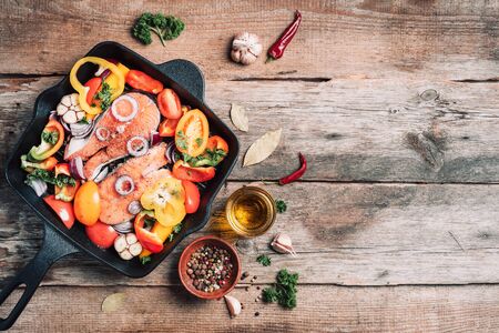 Salmon steak with vegetables on grill pan over wooden background. Top view. Raw salmon fillet with cooking ingredients: oil, herbs, spoon and fork. Banner, copy space.の写真素材