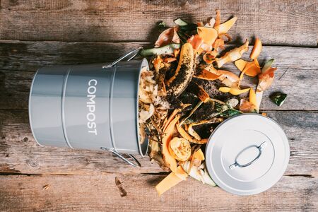 Recycle kitchen waste. Sustainable and zero waste living. Vegetable waste in recycling compost pot. Top view. Copy space. Peeled vegetables on chopping board, white compost bin on blue backgroundの写真素材