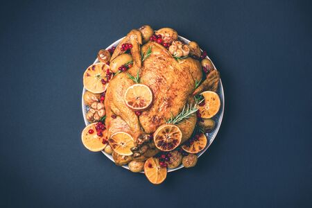 Roasted chicken with oranges, rosemary and cranberries on plate over concrete background. Traditional Thanksgiving or Friendsgiving holiday celebration dish. Friends or family dinner. Festive Christmas tableの写真素材
