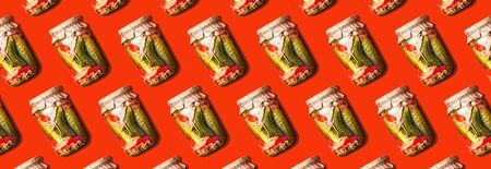 Canned and preserved vegetables in glass jars on orange background. Pickled cucumbers in jar pattern. Top view. Flat lay. Creative packing design. Healthy fermented food concept.の写真素材