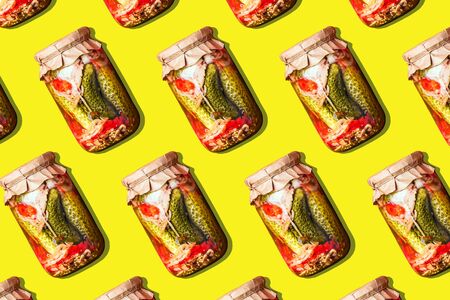 Canned and preserved vegetables in glass jars on yellow background. Pickled cucumbers in jar pattern. Top view. Flat lay. Creative packing design. Healthy fermented food concept.の写真素材