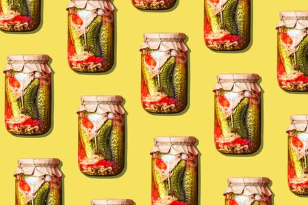 Canned and preserved vegetables in glass jars on yellow background. Pickled cucumbers in jar pattern. Top view. Flat lay. Creative packing design. Healthy fermented food concept.の写真素材