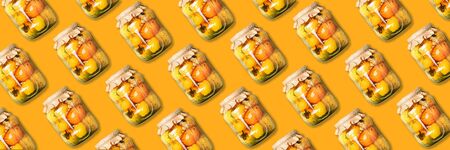 Pickled tomatoes in jar pattern on orange background. Top view. Creative packing design. Canned and preserved vegetables. Ingredients for vegetables preserving. Healthy fermented food conceptの写真素材
