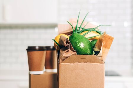 Craft paper cups with coffee to go and food box, lunch on tabletop over white kitchen. Banner, copy space. Safe delivery, take away only concept. Food delivery service during coronavirus pandemic.の写真素材