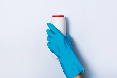Hand in glove holding white plastic bottle of cleaning product, household chemicals. Copy space. Cleaning service concept. Household chemical cleaning products, brushes and supplies. Detergent bottle.の写真素材