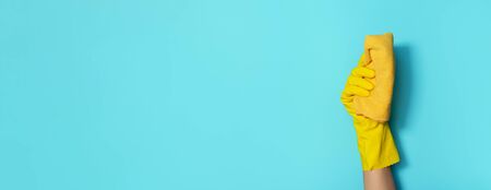 Hand in glove holding microfiber cleaning cloth on blue background. Copy space. Cleaning service...