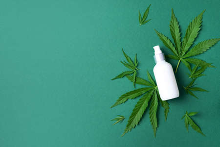 Hemp cosmetic products white bottles with oil, hemp seed extract, cream and cannabis leaves on green background. Flat lay. Top view. Copy space. Natural skin care and body treatmentの写真素材