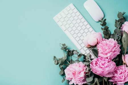Home office workspace with white keyboard, notebook and peony, eucalyptus flower, copy space on blue background. Feminine workspace. Flat lay. Blogger, business concept. Mock up. Birthday, Woman day.の写真素材