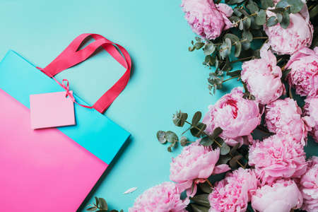 Pink peonies, eucalyptus flowers, gift bags with presents on blue background. Copy space. Flat lay, top view. Floral composition. Wedding, birthday, anniversary bouquet. Woman day, Mothers day.の写真素材