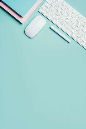 Home designer office workspace. White mouse, keyboard, notebook, pen on blue background. Top view....