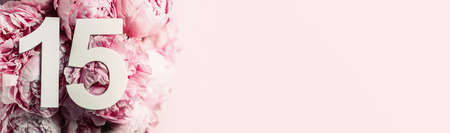 Creative layout. Peony flowers, digit fifteen. Birthday greeting card with inscription 15. Anniversary concept. Top view. Copy space. Stylish white numeral on flower background. Numerical digitの写真素材