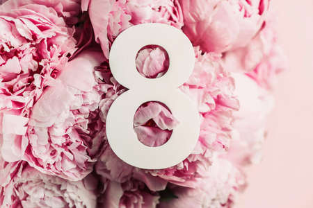 8 March. Happy Womens Day. Creative layout. Pink peony flowers and digit eight 8. Birthday greeting card. Anniversary concept. Top view. White numeral over flowers background. Numerical digit.の写真素材
