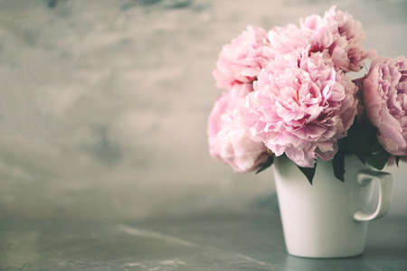 Pink peony flowers in white cup on marble vintage background. Wedding, birthday, anniversary bouquet. Copy space. Trendy pastel floral composition. Woman day, Mothers day. Macro of peonies flowersの写真素材
