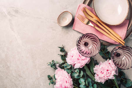 Flat lay composition with peony, eucalyptus flowers, empty plates, napkin, golden cutlery, wineglasses for serving a festive table, dinner on marble background. Copy space. Top view. Table setting.の写真素材