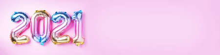 Colorful foil balloons made numbers 2021 on pink background with light bokehs. Banner, copy space....