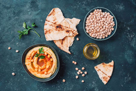 Chickpeas hummus, olive oil, raw chickpeas, smoked paprika, pita on dark background. Middle eastern, jewish cuisine or arabic dishes. Top view. Copy space. Snacks set. Vegan, vegetarian food conceptの写真素材