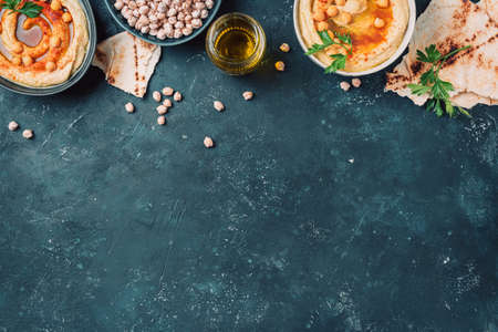 Chickpeas hummus, olive oil, raw chickpeas, smoked paprika, pita on dark background. Middle eastern, jewish cuisine or arabic dishes. Top view. Copy space. Snacks set. Vegan, vegetarian food conceptの写真素材
