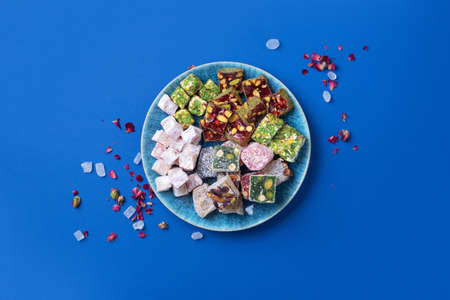 Middle Eastern sweets. Turkish delight with pistachios nuts on plate over blue background. Top view. Copy space. Arab dessert, rahat lokum, sherbet, nougat, churchkhela, cookies. Flat lay.の写真素材