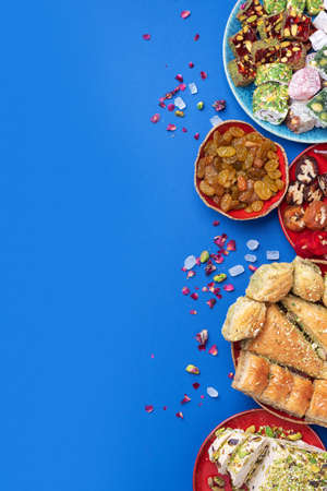Middle Eastern sweets on blue background. Arab dessert, baklava, halva, rahat lokum, sherbet, nuts, pistachios, dates, raisins, dried apricots, churchkhela, cookies. Top view. Flat lay. Copy spaceの写真素材
