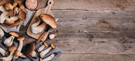 Fresh forest boletus mushrooms on wooden background. Top view. Copy space. Autumn harvest concept. Banner. Fresh picked Porcini mushrooms in basketの写真素材