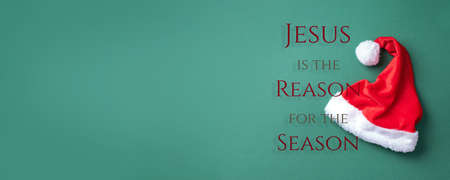 Red Santa Claus hat on green background. Top view. Copy space. Advent time. Christmas greeting card. Remember the real Reason of the Season. Christian Christmas concept. Jesus Christ bornの写真素材