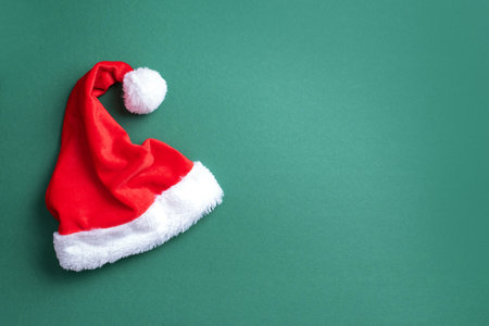 Red Santa Claus hat on green background. Top view. Copy space. Advent time. New year composition. Decoration for winter holidays celebration. Christmas greeting cardの写真素材