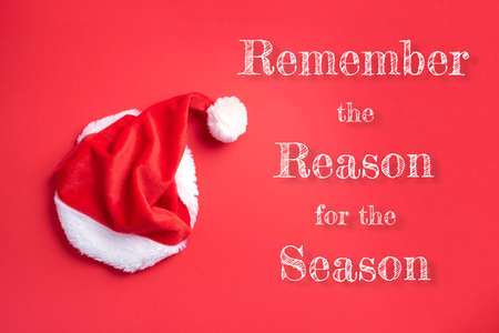 Red Santa Claus hat on red background. Top view. Copy space. Advent time. Christmas greeting card. Remember the real Reason of the Season. Christian Christmas concept. Jesus Christ bornの写真素材