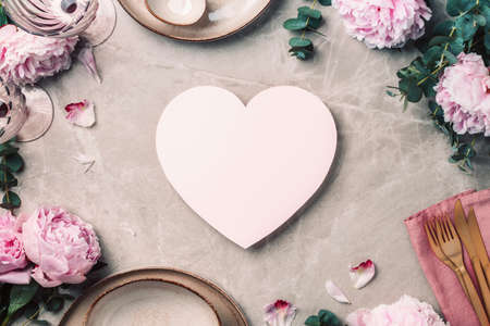 Flower arrangement on table served for festive dinner with copy space for your text, invitation. Greeting card. Top view. Peony, eucalyptus, plates, golden cutlery, wineglasses on marble backgroundの写真素材