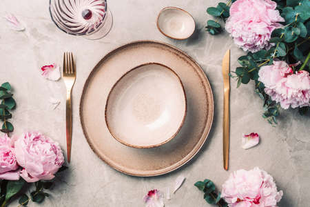 Flat lay composition with peony, eucalyptus flowers, empty plates, napkin, golden cutlery, wineglasses for serving a festive table, dinner on marble background. Copy space. Top view. Table settingの写真素材