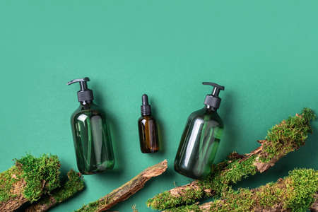 Green glass bottle of shampoo, soap, conditioner on green background with natural moss over bark, wood. Top view, copy space. Blank label for mock-up. Skin care, organic body treatment, spa conceptの写真素材