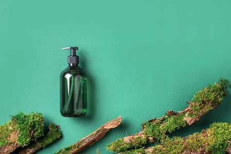 Unlabelled cosmetic bottle on green background, natural moss over branches, bark. Skin care, organic body treatment, spa concept. Vegan eco friendly cosmetology product. Organic cosmetics.の写真素材