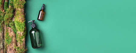 Green glass bottle of shampoo, soap, conditioner on green background with natural moss over bark, wood. Top view, copy space. Blank label for mock-up. Skin care, organic body treatment, spa conceptの写真素材